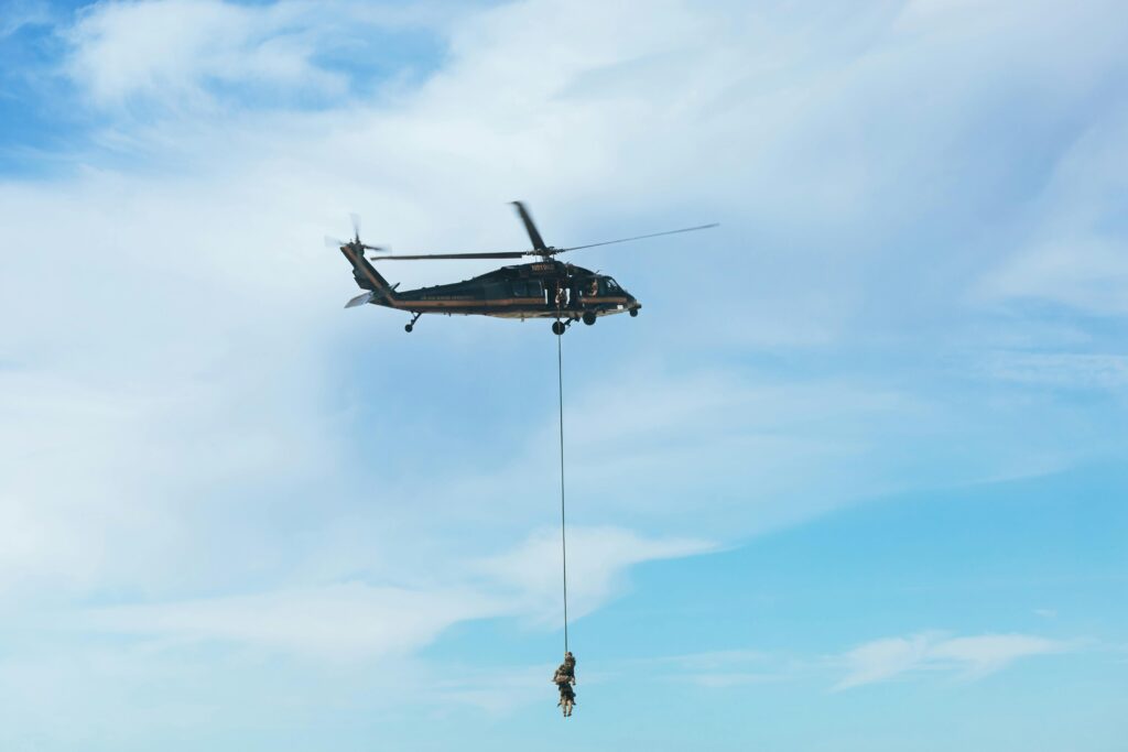 Military personnel practice a helicopter rescue operation involving rappelling from a flying aircraft.